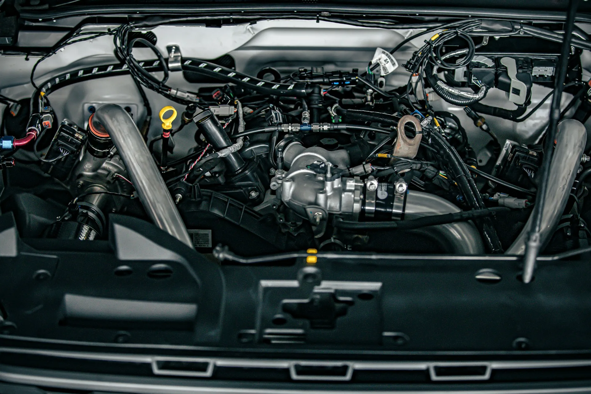 Engine bay of a modern car seen from the front, with wiring harnesses, connectors and control units routed around the engine.